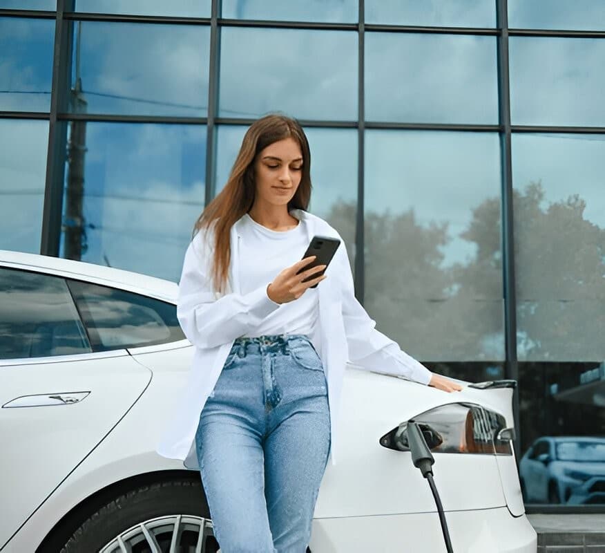 A lady standing beside a tesla using her phone